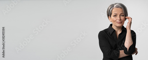Adult woman in black shirt isolated on white background holds her hand near face. Pretty Grey haired woman next to copy space. High quality photo.