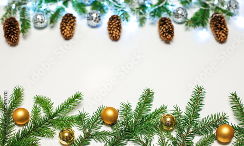 Christmas composition with fir branches and Golden ornaments balls on a blurry background with cones and lights of garlands