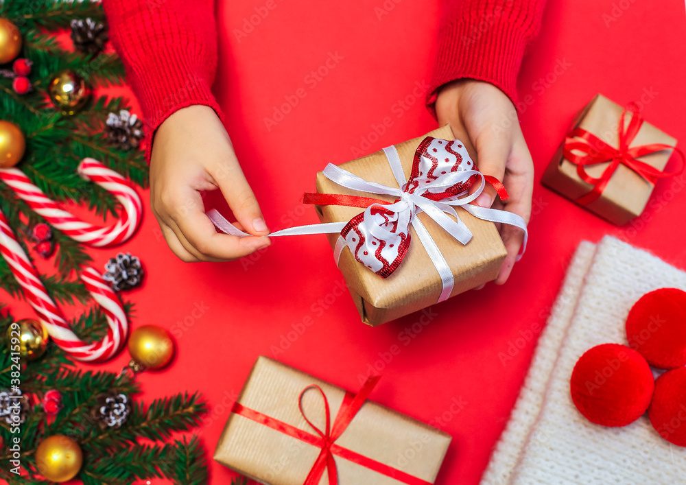 Christmas gifts, children's hands open a new year's gift on a red background, Christmas composition fir branches with gifts, gold-colored decorations, red balls and caramel on a red surface Christmas gifts, children's hands open a new year's gift on a red background, Christmas composition fir branches with gifts, gold-colored decorations, red balls and caramel on a red surface