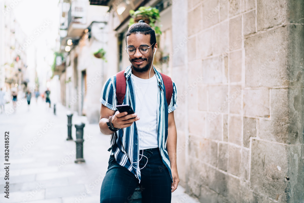 Cheerful man with earphones using smartphone on street
