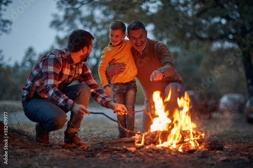 Obraz na płótnie Grandfather, father and son camping together; Spring or autumn camping with campfire at night ; camping, travel, tourism, hike and people concept