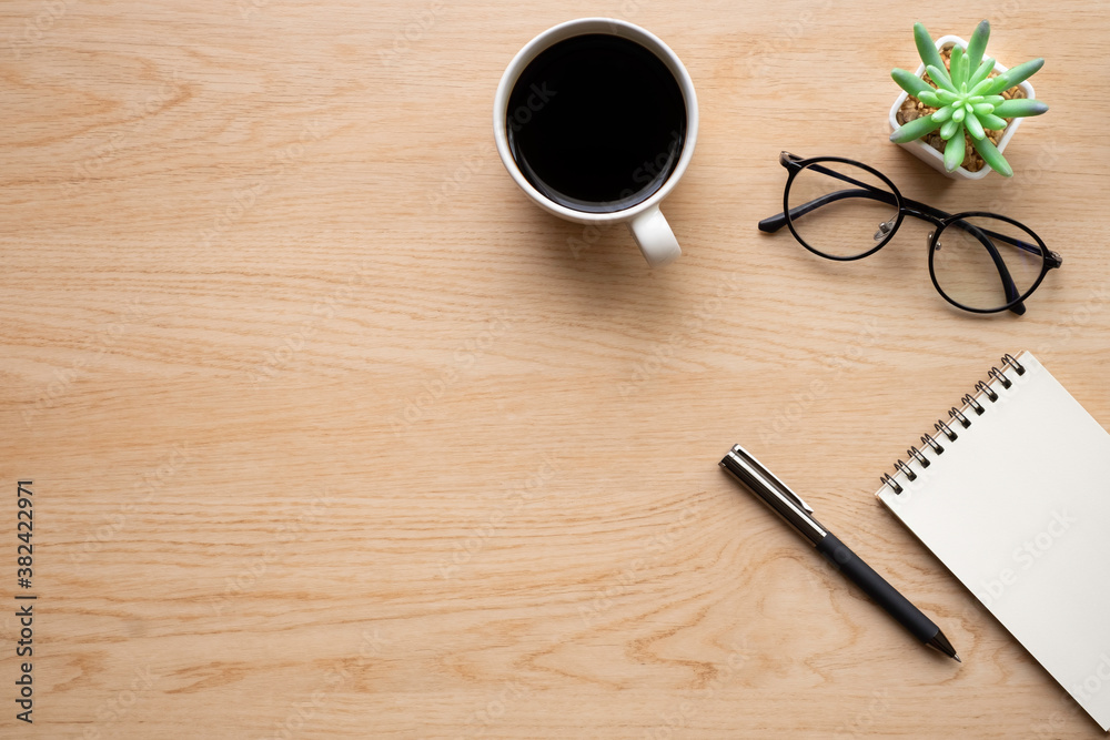 Top view above of Wooden office desk table with blank notebook, pen and coffee cup with glasses. Business and finance concept. Workplace, Flat lay with blank copy space. Top view above of Wooden office desk table with blank notebook, pen and coffee cup with glasses. Business and finance concept. Workplace, Flat lay with blank copy space.