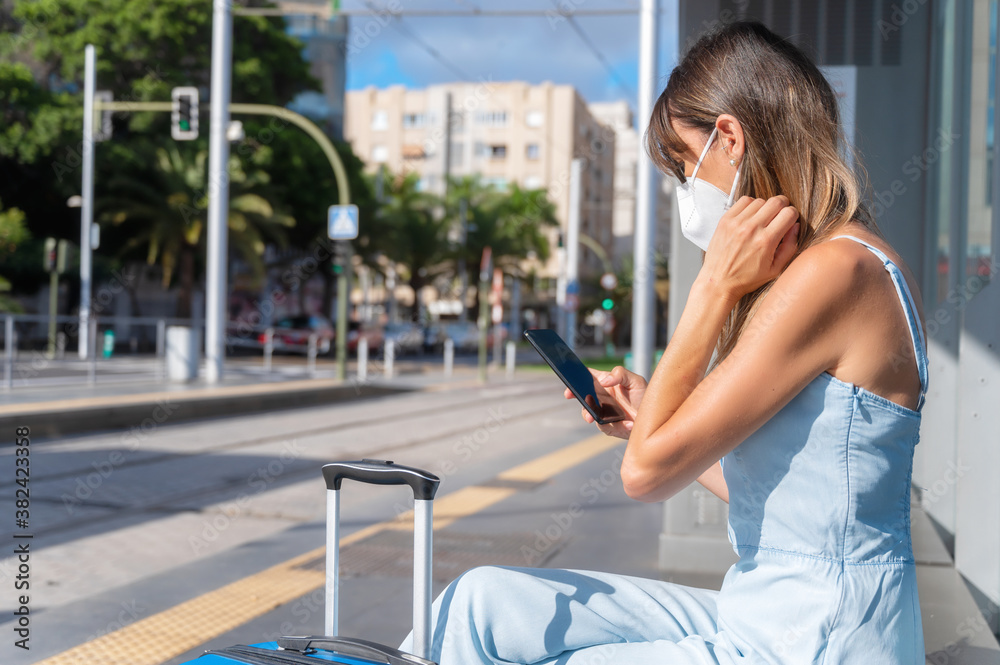 Commuting in the city during new normal. Woman with protective face mask against Coronavirus outbreak waiting at tram station. High quality photo