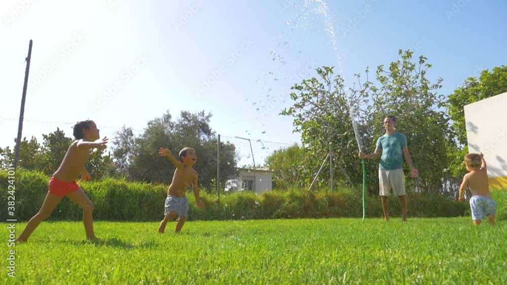 Father playing with his sons in the garden with the hose and water. Watering and playing together in a funny way. Father playing with his sons in the garden with the hose and water. Watering and playing together in a funny way.