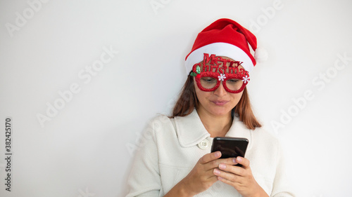 A woman with Merry Christmas glasses is holding a phone for a zoom in or online shopping.