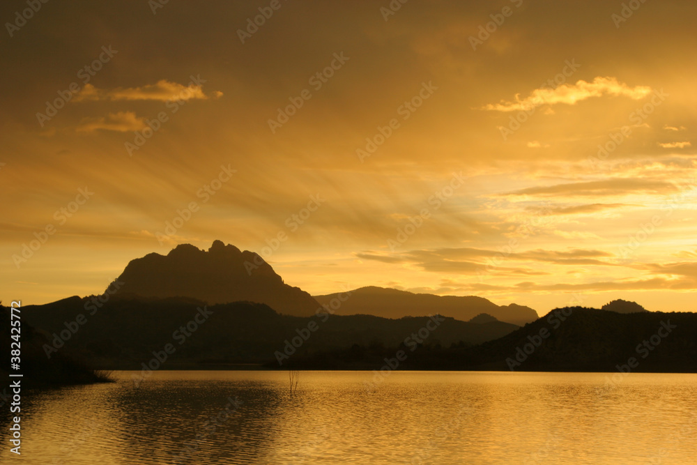 Fototapeta premium Amanecer en un pantano, con montañas al fondo y cielo con nubes. Pantano del Quípar, Calasparra (Murcia).