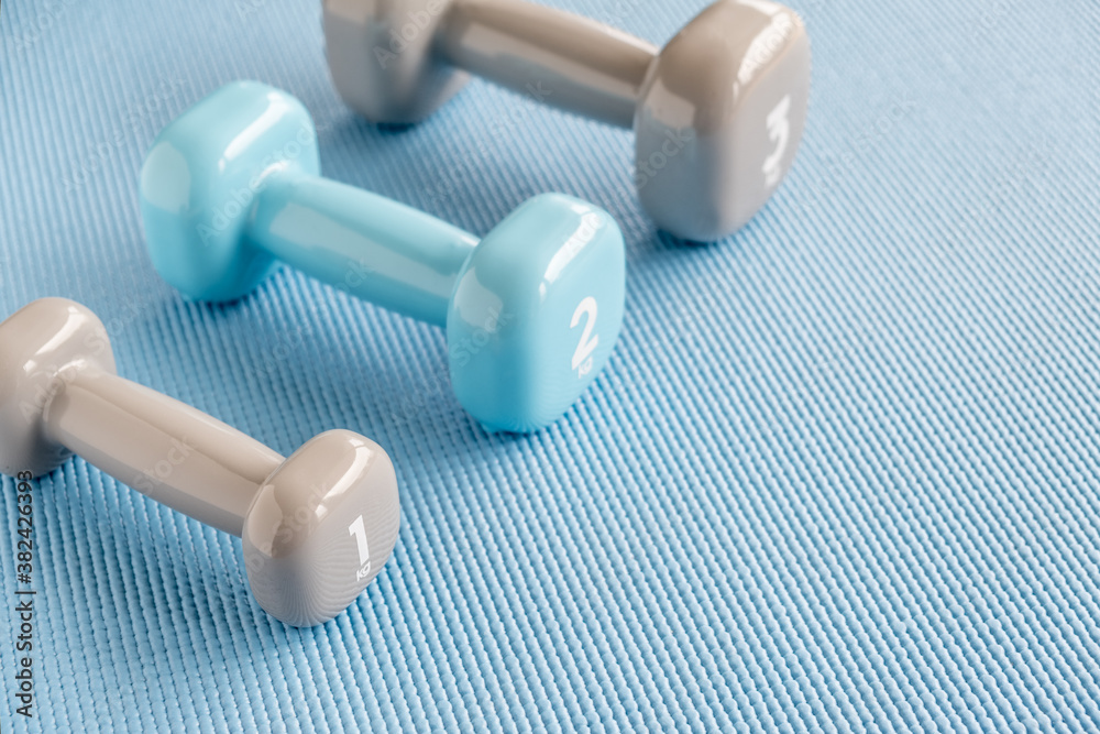 Set of blue and grey dumbbells on the blue fitness mat, close up Set of blue and grey dumbbells on the blue fitness mat, close up