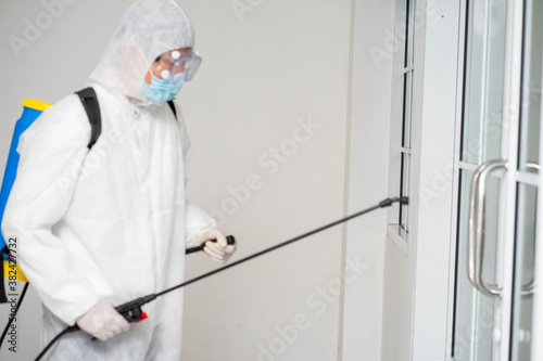 health care worker in white jumpsuit and protective face mask using spraying machine to disinfect virus pandemic.  Health care and midicine concept. New normal social distancing concept. © ake