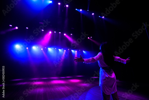 Unrecognizable singer standing on stage at microphone, back view, neon lights © nagaets