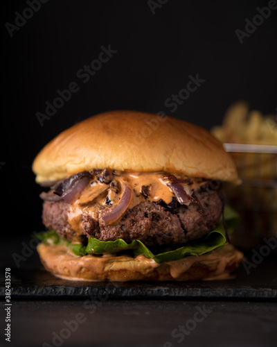 Closeup of a  fresh juicy burger with lettuce, onions and cheese on black background photo