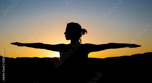 Silhouette of a woman against a beautiful sunset background. a Woman stretches her hands and doing yoga meditation exercise.