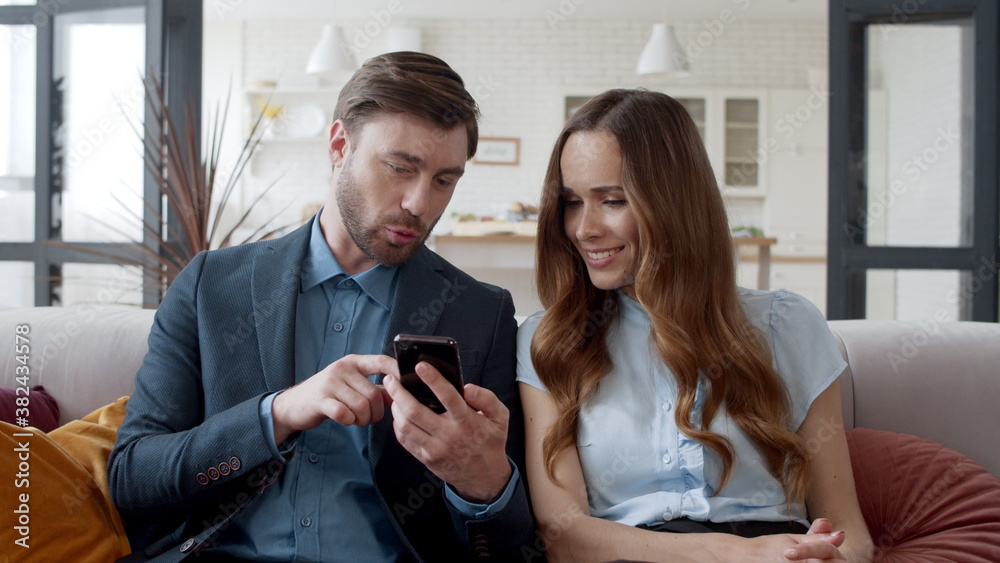 Smiling couple looking mobile phone at home office. Laughing man and woman. Smiling couple looking mobile phone at home office. Laughing man and woman.