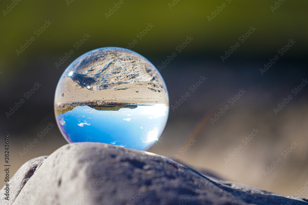 Photography Crystal Photo Ball showing upside down reflection of sky beach and waves balanced on rocks on sandy beach. Photography Crystal Photo Ball showing upside down reflection of sky beach and waves balanced on rocks on sandy beach.