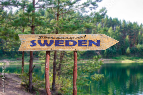 Sweden wooden arrow road sign against lake and pine trees background. Travel to Sweden concept. photo