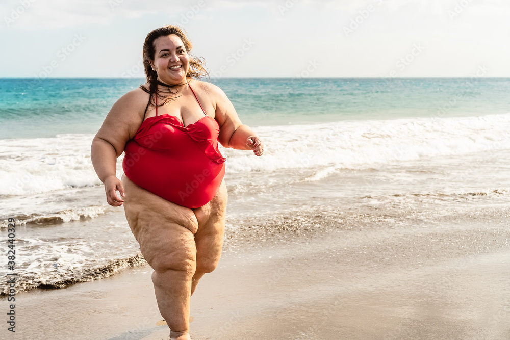 Happy plus size woman running on the beach - Curvy overweight model having fun during vacation in tropical destination - Over size confident person concept