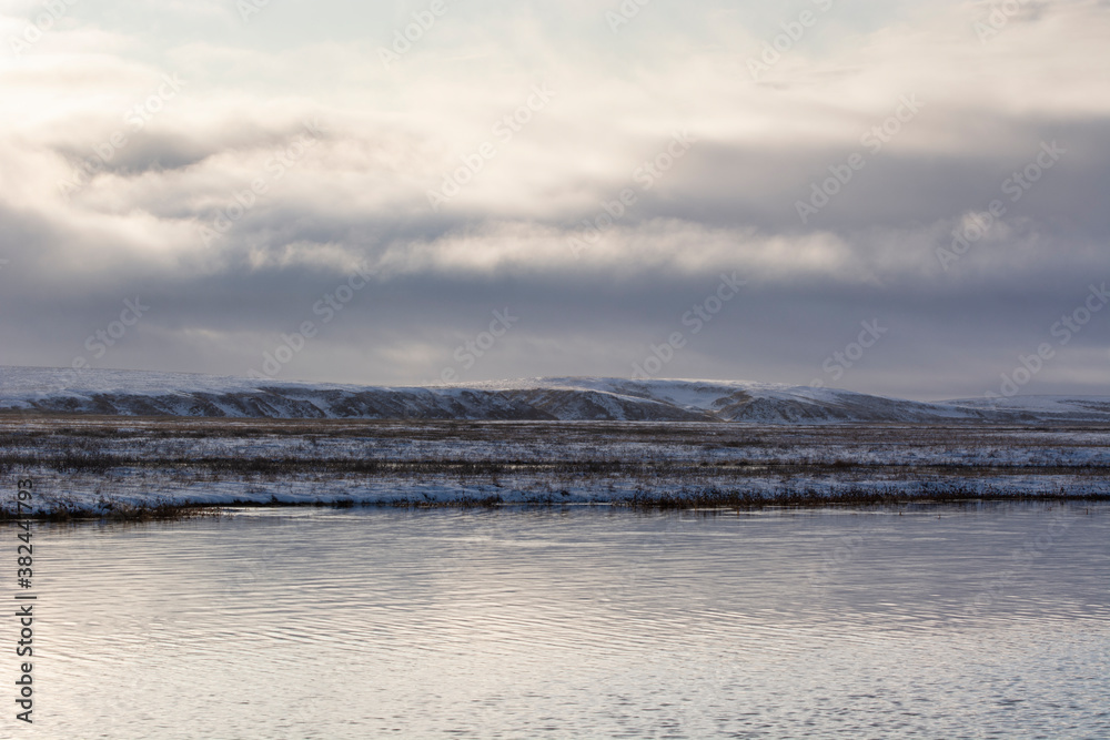 autumn landscape with a lake in the tundra on the background of snow clouds