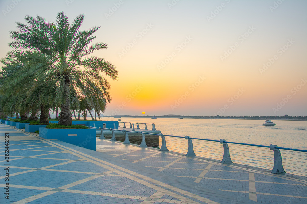The view of the Persian Gulf, Corniche promenade with palm trees on sunset in Abu Dhabi, United Arab Emirates