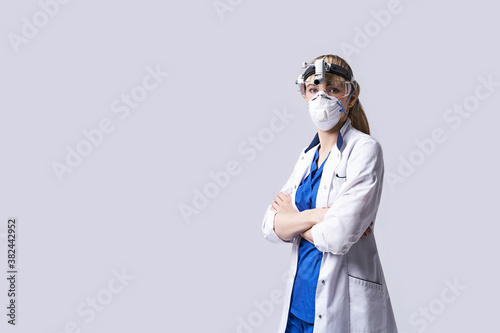 Confident ENT doctor wearing surgical headlight head lantern, protective face mask and glasses. Portrait of female otolaryngologist standing arms crossed on light grey background. photo