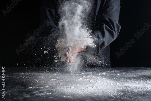 Chef claps white flour, man hand on black background