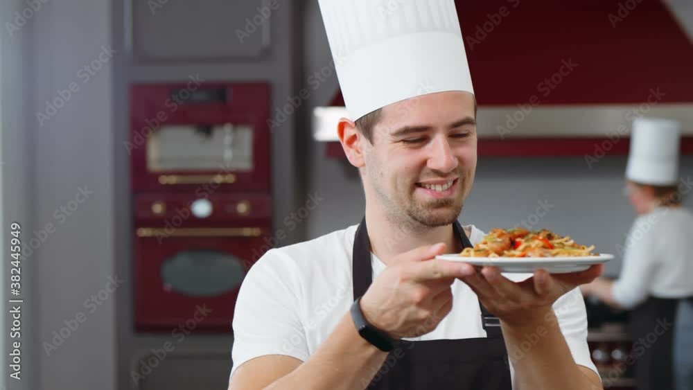 Smiling happy chef standing in kitchen and holding plate with delicious healthy dish Smiling happy chef standing in kitchen and holding plate with delicious healthy dish