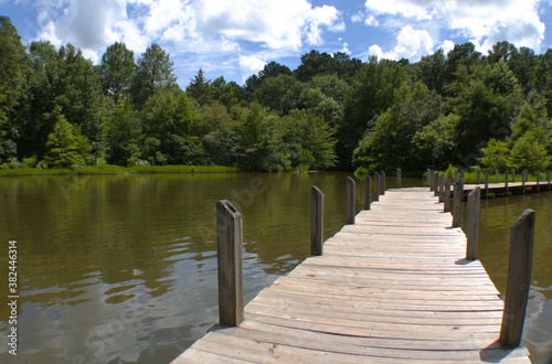Wooden fishing pier next to green forest lined lake.