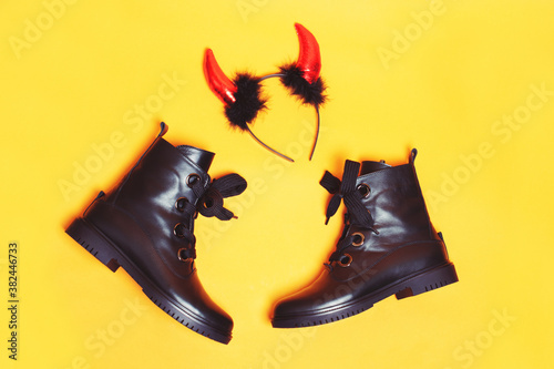 Black shiny leather witch shoes with big funny laces and red sparkling devil horns on orange background creating festive mood of a holiday. Halloween party preparation and decoration concept. photo