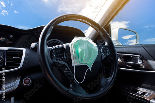 Surgical face mask placed on steering wheel in a car , Coronavirus (COVID-19) prevention concept