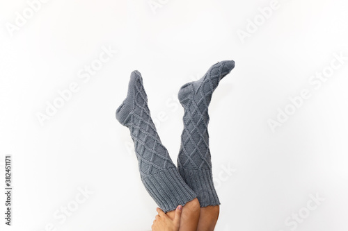 Gray knitted knee socks on the legs on a white background. Legs in long socks upside down. A beautiful knitted product for a gift. We knit with our own hands. Hobby