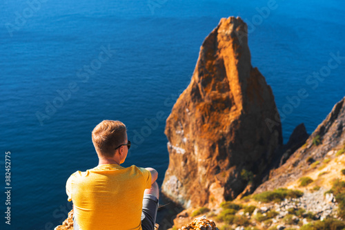 Young man in yellow clothes sitting high above the sea, against the background of coastal rocks, calm clear blue sea, Cape Fiolent in Crimea. photo