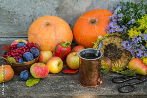 Copper mug with tea against the background of the autumn harvest of pumpkins  apples  plums  pears and viburnum on a wooden table. Vintage rustic style