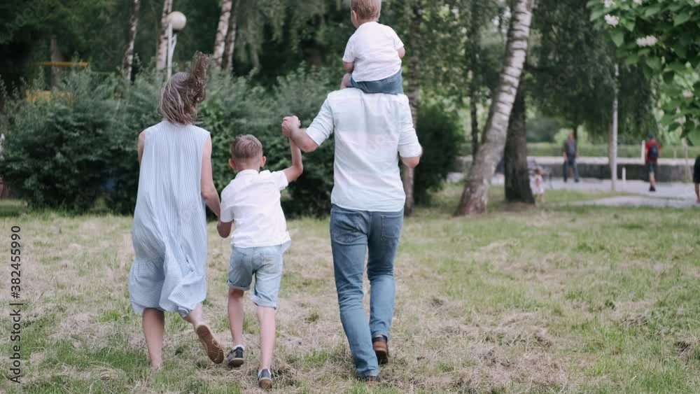 Parents are outside with kids. They are happy together. The father is carrying a son on shoulders. Parents are outside with kids. They are happy together. The father is carrying a son on shoulders.