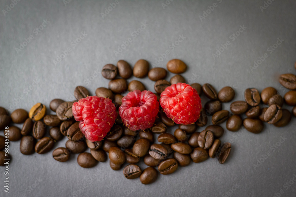 Kaffeebohnen mit drei Himbeeren auf grauem Hintergrund Kaffeebohnen mit drei Himbeeren auf grauem Hintergrund