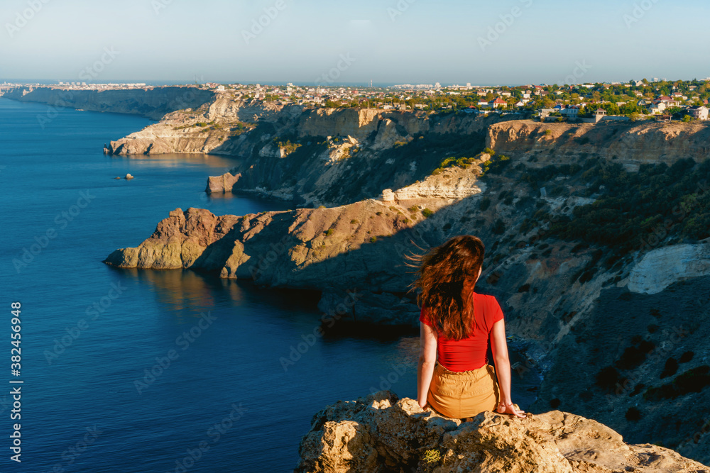 Rear view of traveler woman standing on cliff edge in front of amazing seascape. Freedom, travel and vacation concept. - obrazy, fototapety, plakaty 
