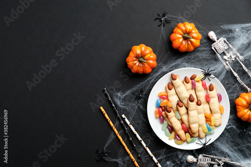 Halloween pastry concept. Halloween cookie in shape of witch fingers with almonds nails, pumpkins, spider webs, skeletons on black background