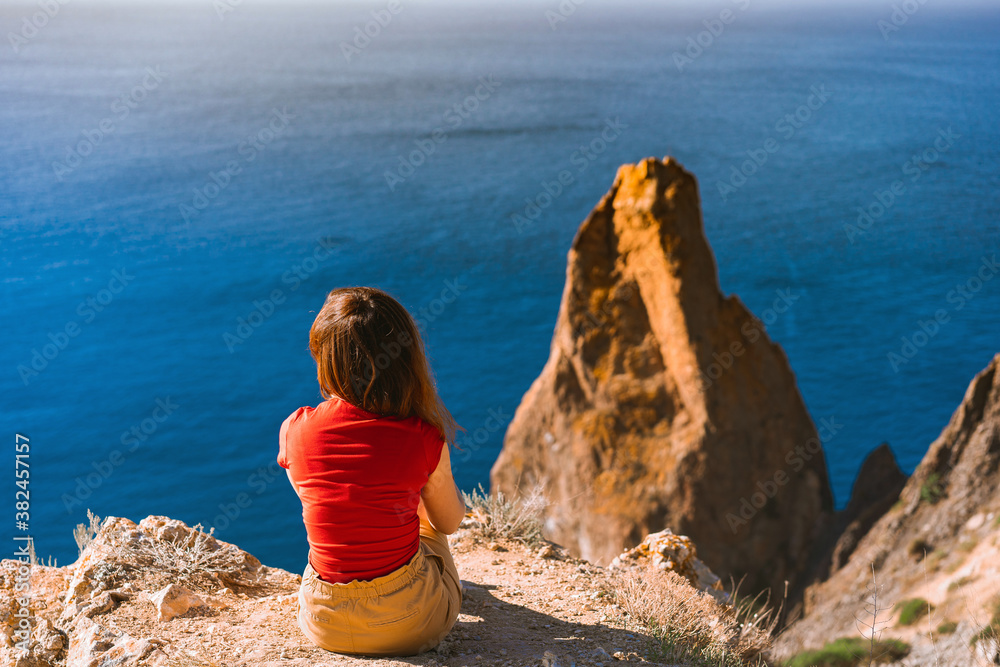 Rear view of traveler woman standing on cliff edge in front of amazing seascape. Freedom, travel and vacation concept.