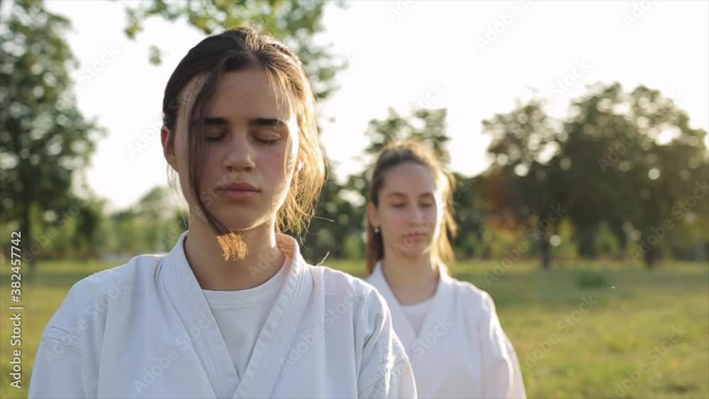 Karate sportswomen meditate in nature and one of the girls opens her eyes and looks at the camera. Close-up. Slow motion. The camera zooms out and changes focus Karate sportswomen meditate in nature and one of the girls opens her eyes and looks at the camera. Close-up. Slow motion. The camera zooms out and changes focus