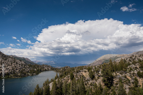 An alpine lake with trees  mountains and dramatic  stormy clouds on a sunny day.