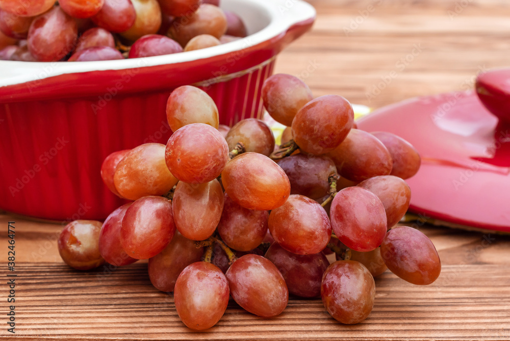 Obraz premium Ceramic pot with red grapes on wooden table.