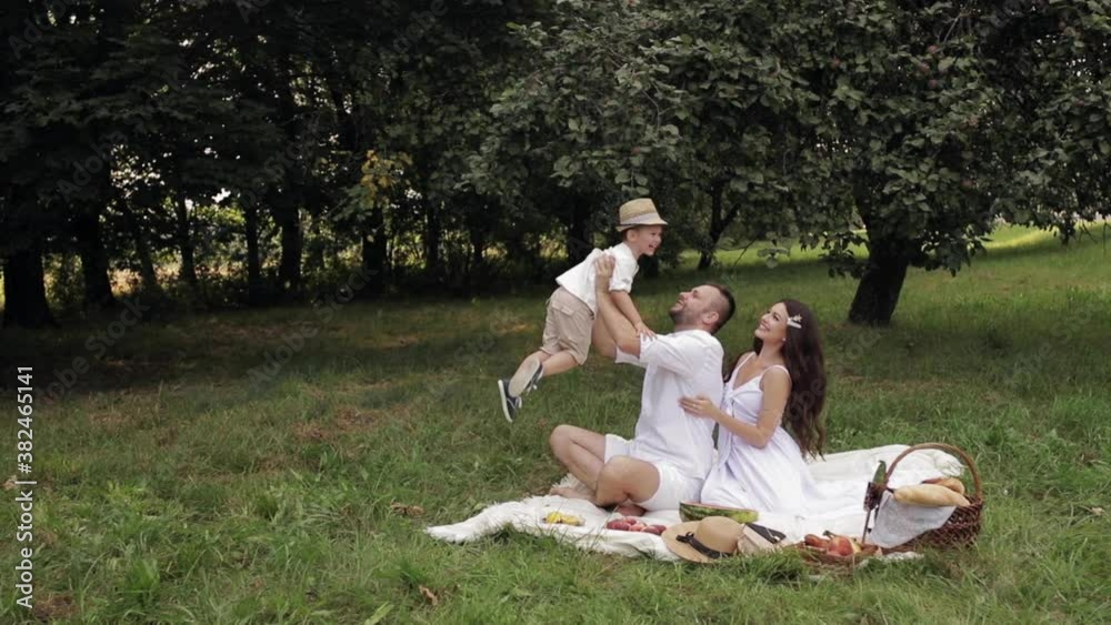Beautiful dad and mum with long hair with their child spend a lot of time together and have fun in the park in summer Beautiful dad and mum with long hair with their child spend a lot of time together and have fun in the park in summer