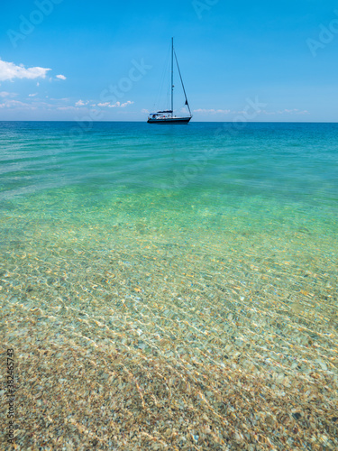 alone sailing yacht at emerald calm sea under blue sky