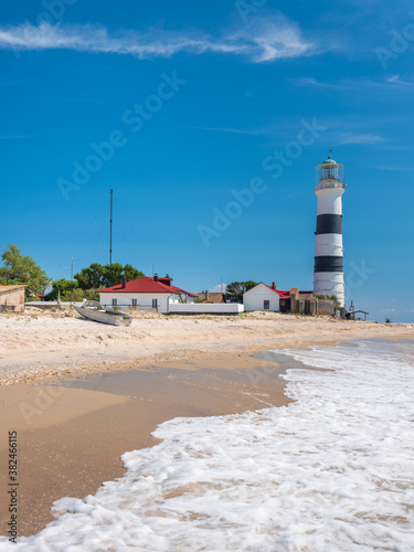 view to white foam of waves and lighthouse on the beach in summer day with copy space in the sky