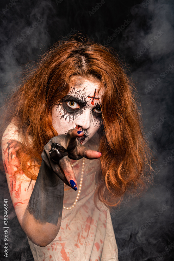 A young woman with red hair and professional make-up to look creepy, wearing bloody white clothes. On a black background