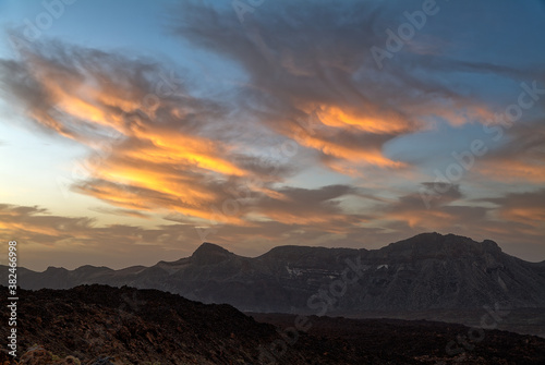 Beautiful orange clouds in the sky over the caldera in the Teide region on the island of Tenerife in the early morning before sunrise. The ground resembles a lunar landscape.