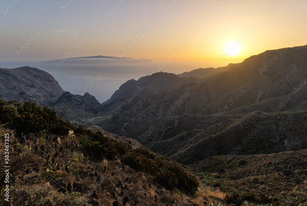 View through a valley of the Teno Mountains on the island of Tenerife at sunset. In the distance the Atlantic Ocean and on the horizon the neighboring island of La Gomera surrounded by clouds.