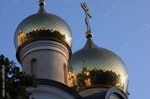 View of the top of the Orthodox Church Of Matrona of Moscow with shining domes and a cross.Ensemble of two Golden towers glowing with morning light against the blue sky close-up.