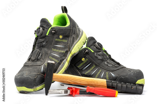 Pair of black work boots with with green lining along with a hammer with wooden handle, a red pliers and a red Phillips screwdriver. With a white background.