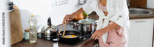 panoramic crop of woman cooking eggs on frying pan in kitchen