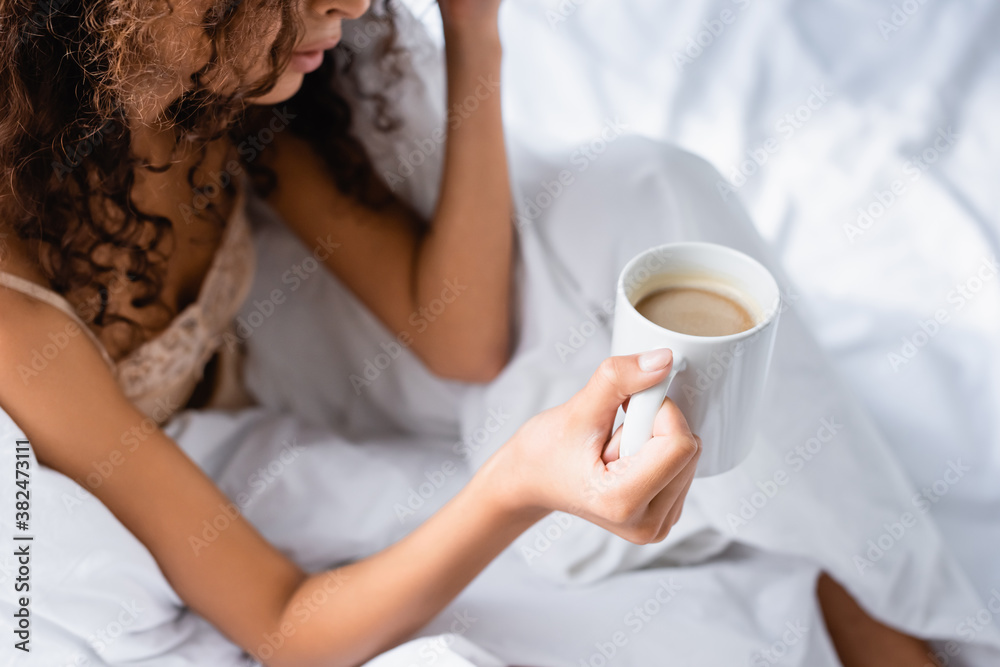 partial view of curly woman holding cup of coffee in morning