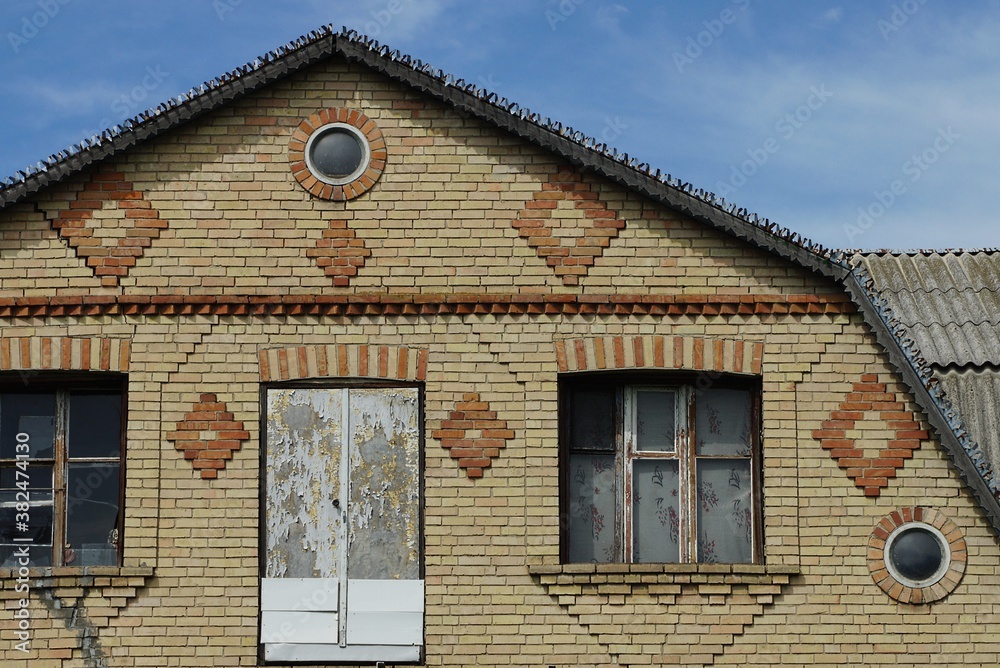 brown brick attic of a rural house with windows and a door on a blue sky background