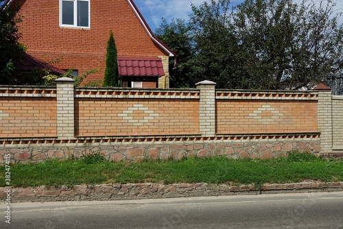 Fototapeta Naklejka Na Ścianę i Meble -  brown long fence of brick and stone in green grass on the street